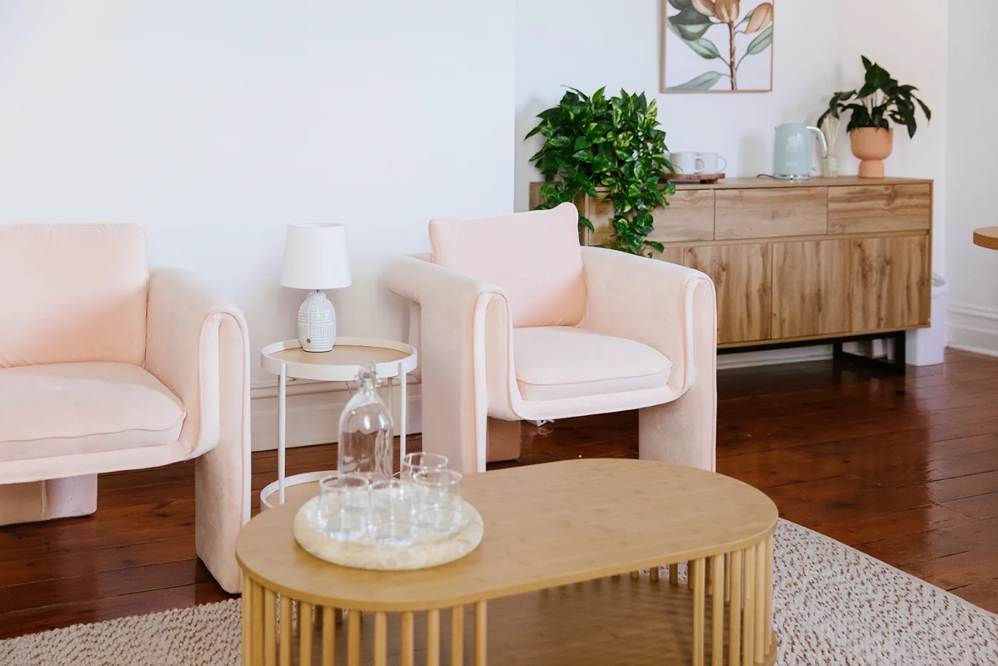 Two blush velvet armchairs beside a low timber table in a calm, sunlit room.
